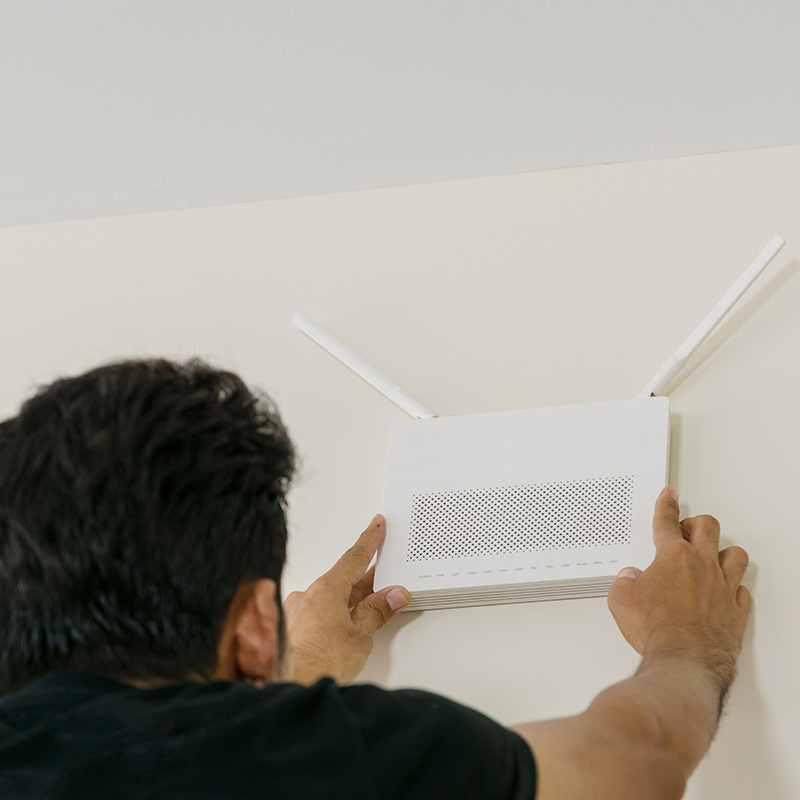 A wireless access point being installed on a ceiling or wall in an office, with employees working on laptops in the background.